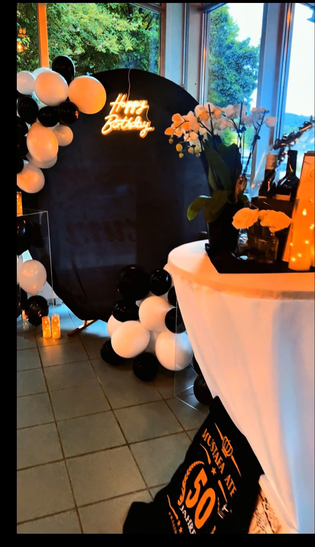Geburtstagskulisse mit schwarzem Rundbogen, Neonschrift, Kerzen und Orchideen